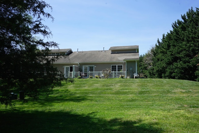 rear view of house featuring a lawn, a shingled roof, and a wooden deck