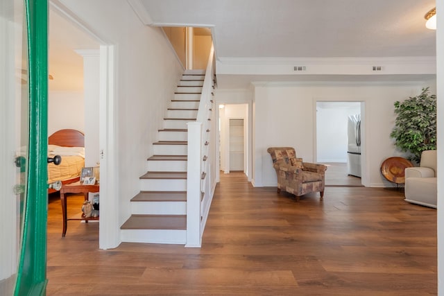 stairs featuring wood finished floors, crown molding, baseboards, and visible vents