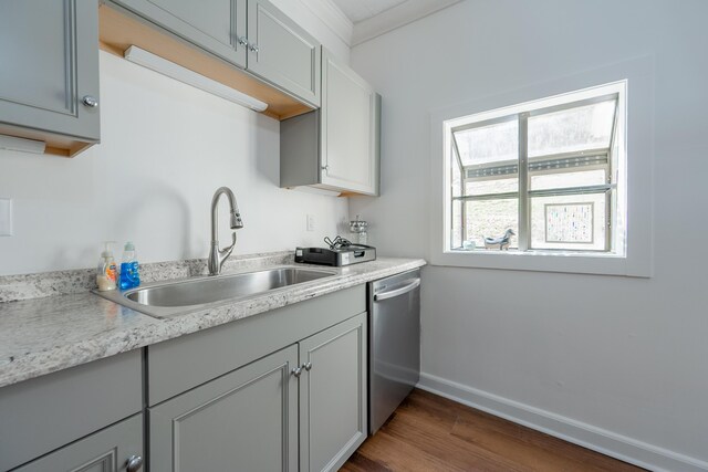kitchen featuring light countertops, baseboards, dark wood finished floors, stainless steel dishwasher, and a sink
