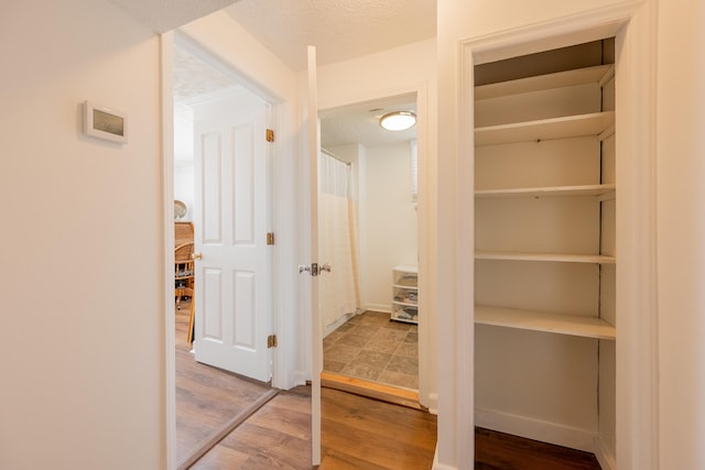 corridor featuring baseboards, wood finished floors, and a textured ceiling