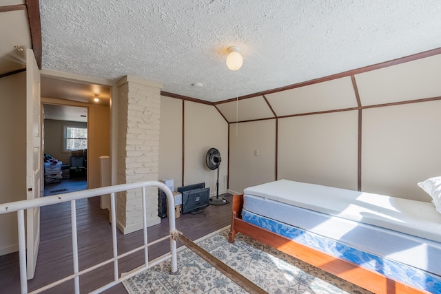 bedroom with vaulted ceiling, wood finished floors, and a textured ceiling