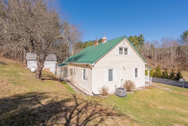 back of property with metal roof, a chimney, central AC, and a yard