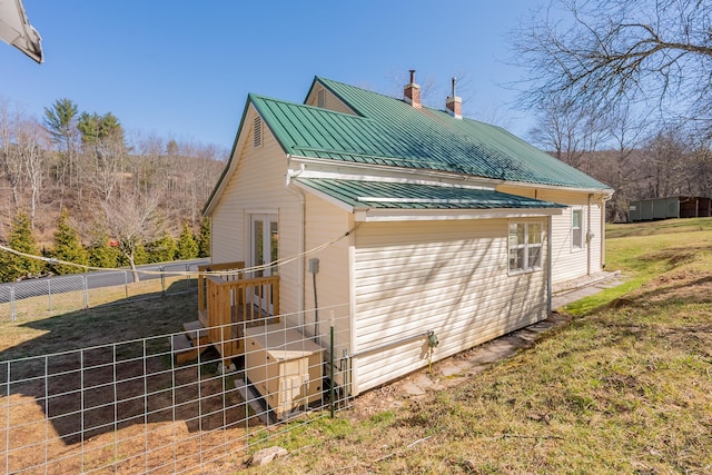 view of home's exterior with a standing seam roof, french doors, a chimney, fence, and metal roof
