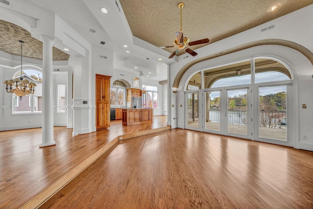unfurnished living room featuring visible vents, light wood-type flooring, decorative columns, recessed lighting, and ceiling fan with notable chandelier