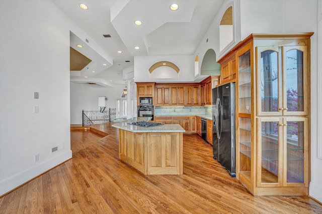 kitchen with light wood-type flooring, black oven, a kitchen island, built in microwave, and refrigerator with ice dispenser