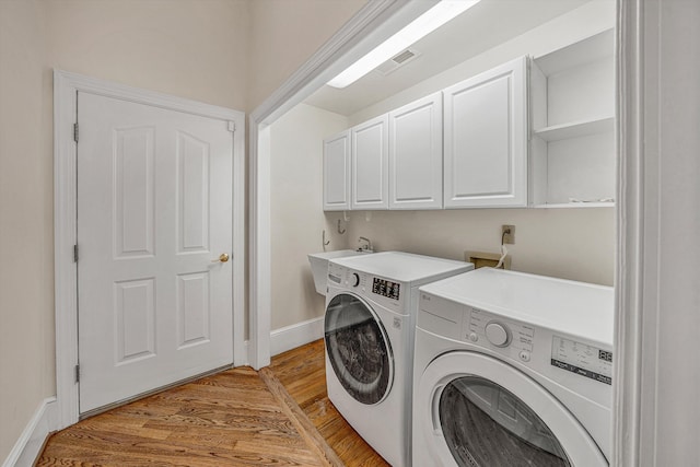 washroom featuring light wood-style flooring, baseboards, a sink, cabinet space, and washing machine and clothes dryer