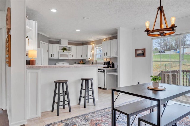 kitchen with white cabinetry, open shelves, a peninsula, a notable chandelier, and white microwave