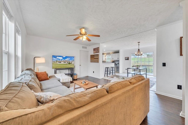 living area featuring a textured ceiling, dark wood finished floors, baseboards, ceiling fan with notable chandelier, and visible vents