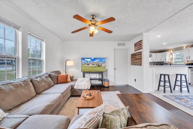 living room with a ceiling fan, visible vents, a textured ceiling, and dark wood finished floors