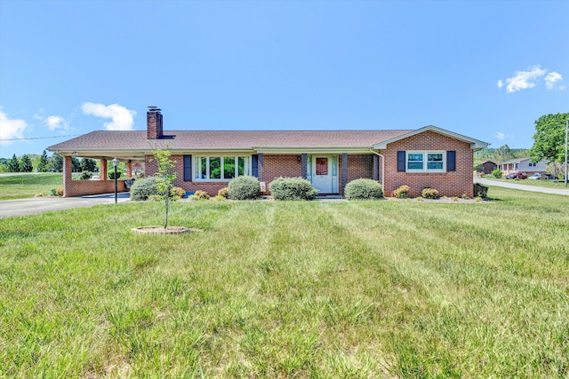 ranch-style house featuring a chimney, a front yard, a carport, brick siding, and aphalt driveway