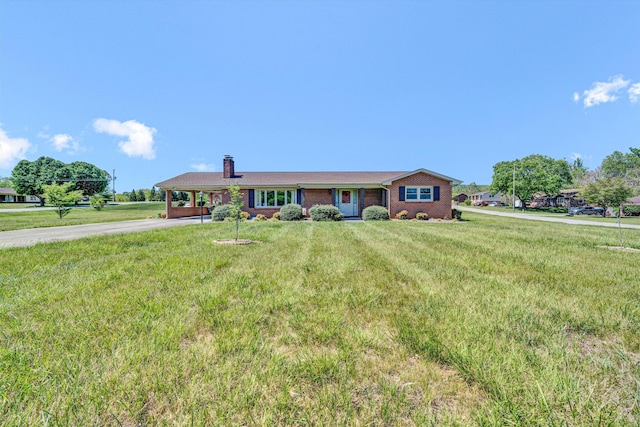 ranch-style house featuring a front yard, a chimney, brick siding, driveway, and a carport