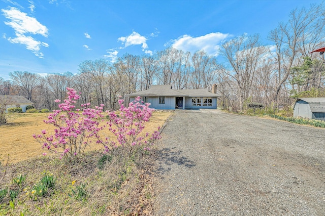 single story home with a garage, an outdoor structure, dirt driveway, a shed, and a chimney