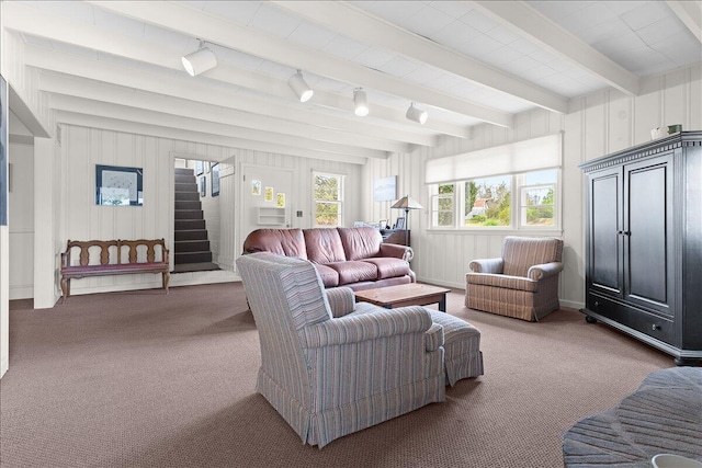 carpeted living area with stairway, rail lighting, and beamed ceiling