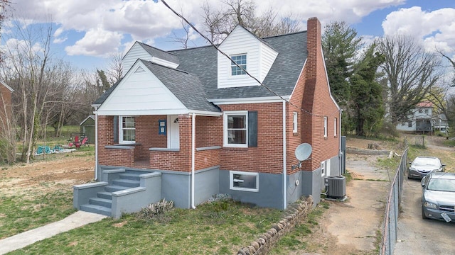 exterior space with central air condition unit, a chimney, brick siding, and roof with shingles