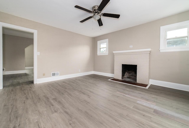 unfurnished living room featuring a brick fireplace, baseboards, visible vents, a ceiling fan, and wood finished floors