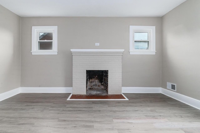 unfurnished living room with wood finished floors, a brick fireplace, baseboards, and visible vents