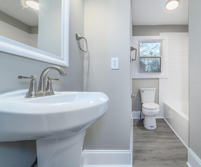 bathroom with toilet, a bathing tub, a sink, wood finished floors, and baseboards