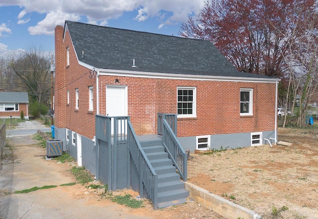 back of property with brick siding, central air condition unit, and roof with shingles