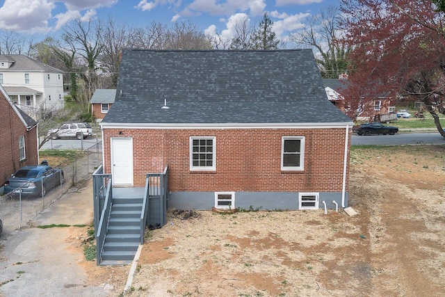 back of property featuring a shingled roof, fence, and brick siding