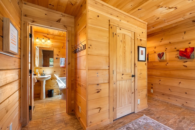 corridor with wooden ceiling, wood walls, and a sink