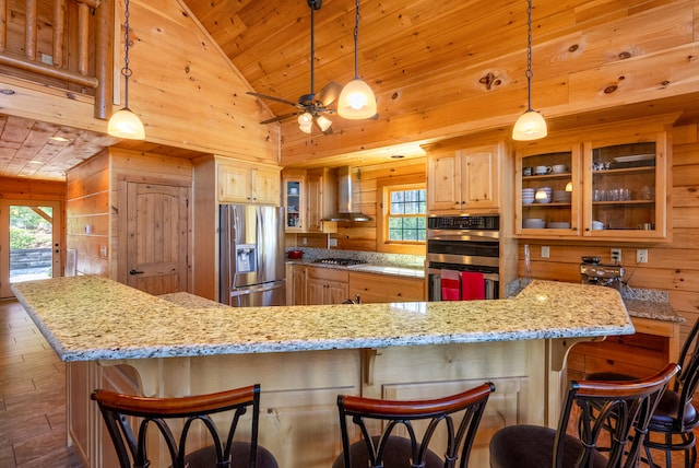 kitchen with wooden ceiling, wall chimney exhaust hood, wood walls, light brown cabinetry, and appliances with stainless steel finishes