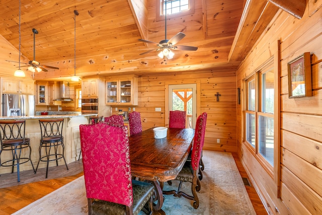 dining space with wooden walls, wood finished floors, wood ceiling, and a ceiling fan