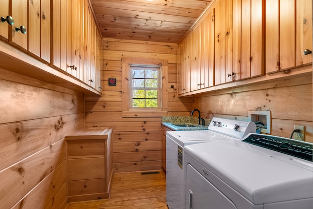 clothes washing area featuring washer and clothes dryer, wooden ceiling, a sink, light wood finished floors, and cabinet space