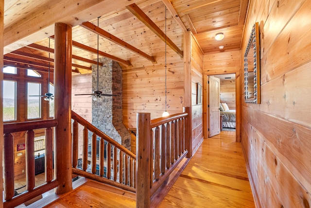 hall with wooden ceiling, an upstairs landing, wood walls, and light wood-style floors