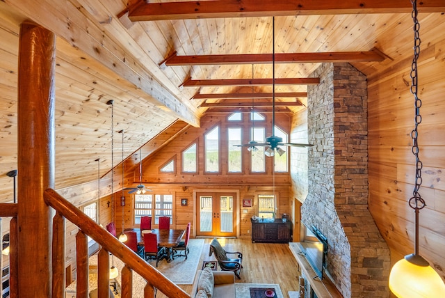 unfurnished living room featuring french doors, wooden walls, beamed ceiling, ceiling fan, and wood finished floors