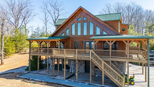 rear view of house featuring stone siding, a wooden deck, stairway, and metal roof