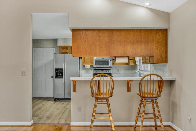 kitchen featuring brown cabinets, a breakfast bar area, light countertops, stainless steel appliances, and a peninsula