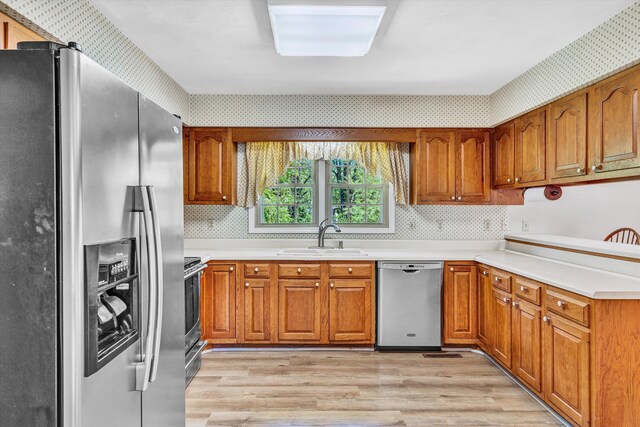 kitchen featuring brown cabinets, stainless steel appliances, a sink, and light wood-type flooring
