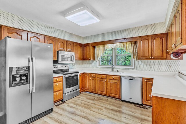 kitchen with light wood-style floors, light countertops, brown cabinets, a sink, and stainless steel appliances