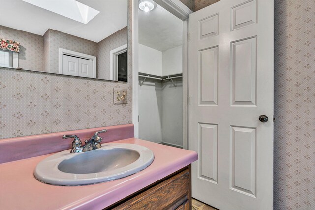 bathroom with wallpapered walls, a skylight, and vanity