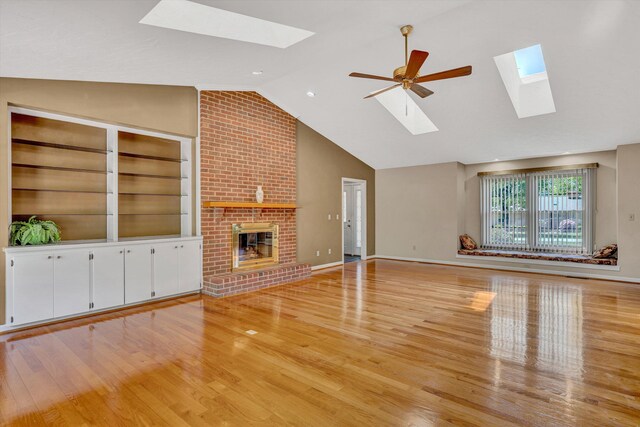 unfurnished living room with a skylight, high vaulted ceiling, a fireplace, and light wood finished floors