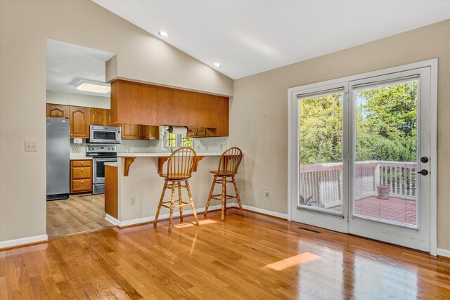 kitchen with a peninsula, light wood-style floors, light countertops, brown cabinets, and stainless steel appliances