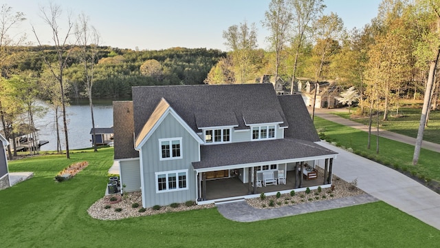 view of front of house with a front yard, a porch, board and batten siding, a view of trees, and roof with shingles