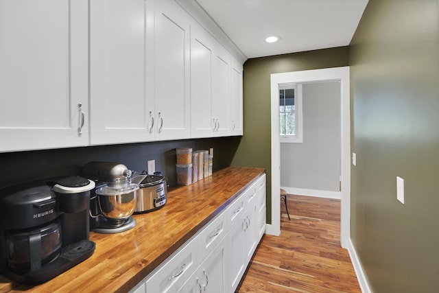 kitchen featuring wooden counters, wood finished floors, baseboards, and white cabinetry