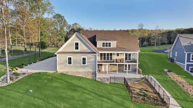 rear view of house featuring a yard, a patio, fence, stone siding, and a balcony