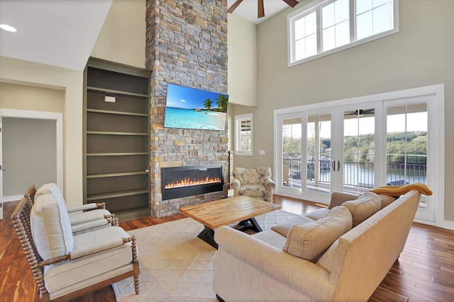 living area featuring wood finished floors, a ceiling fan, a stone fireplace, and a wealth of natural light