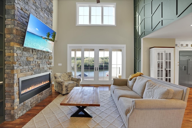 living area with french doors, a towering ceiling, wood finished floors, and a fireplace