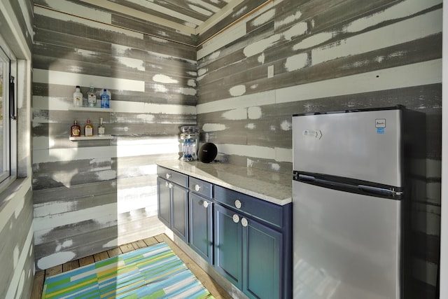 kitchen with blue cabinets, freestanding refrigerator, and wooden walls