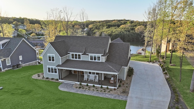 view of front of property featuring board and batten siding, roof with shingles, a forest view, a front lawn, and concrete driveway
