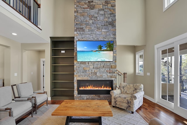 living area featuring a stone fireplace, a towering ceiling, wood finished floors, and baseboards