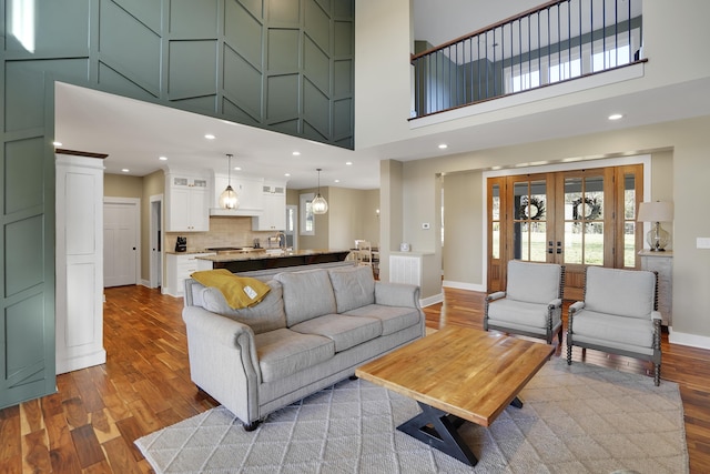 living area with baseboards, recessed lighting, a towering ceiling, and wood finished floors