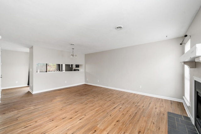 7222 Woods Crossing Dr, Roanoke, VA 24018 - unfurnished living room featuring visible vents, baseboards, a notable chandelier, a fireplace, and light wood-style flooring