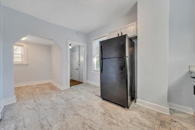 kitchen featuring marble finish floor, freestanding refrigerator, baseboards, and white cabinetry