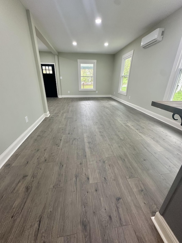 unfurnished living room featuring an AC wall unit, baseboards, dark wood-style flooring, and recessed lighting