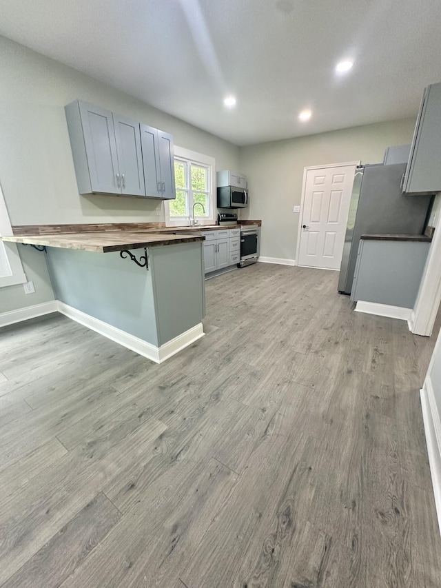kitchen featuring light wood finished floors, stainless steel appliances, a peninsula, baseboards, and wooden counters