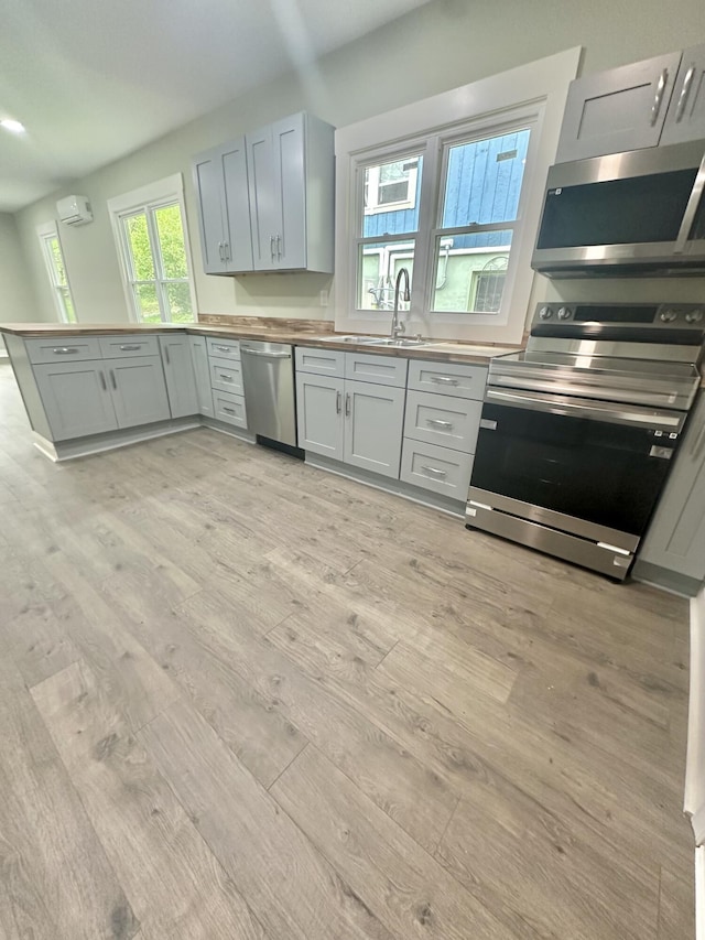 kitchen featuring stainless steel appliances, an AC wall unit, a sink, light wood-type flooring, and wood counters